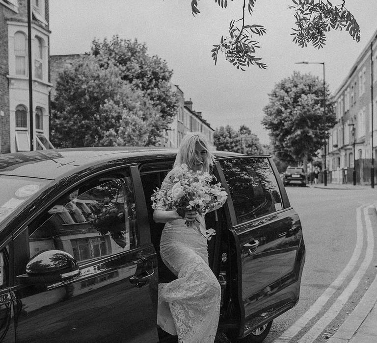 Bride in lace boho two piece and bright mixed floral wedding bouquet stepping out of car to Hackney Studios