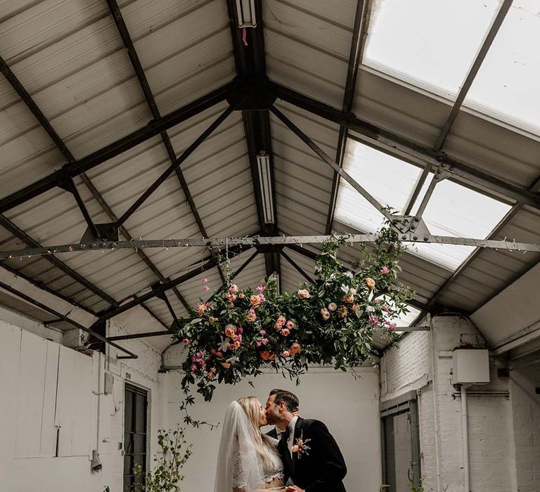 Bride in lace boho two piece and groom in black tux with bow tie and boutonniere sharing kiss at Hackney Studios