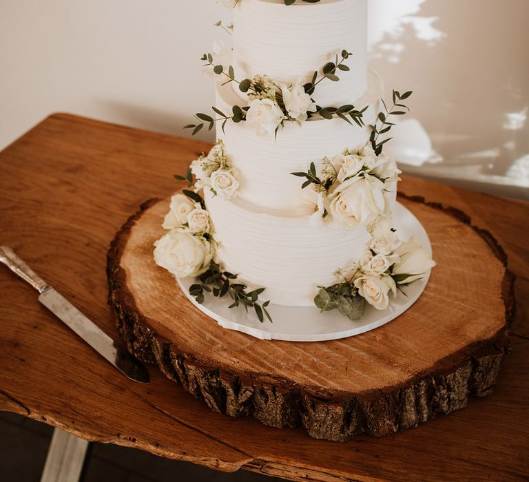 Three tier white frosted wedding cake with greenery decorations and a personalised cake topper 