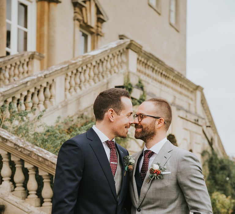 Groom in navy suit jacket and light grey waistcoat with groom in light grey suit jacket and navy waistcoat embrace each other on their wedding day