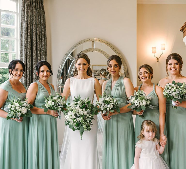 Bridesmaids in sage green dresses in mismatched styles with the bride and flower girl for bridal party portraits 