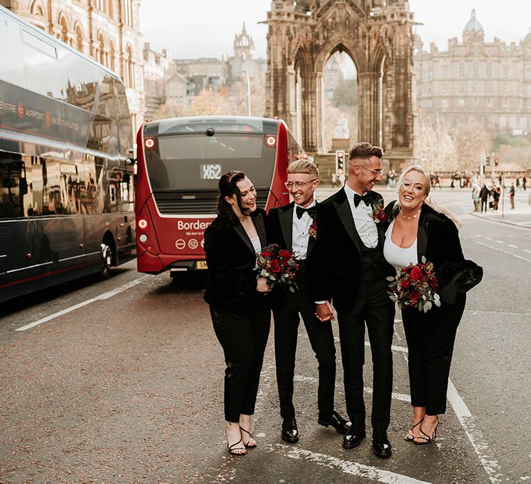 I do crew in matching outfits, black velvet blazers, black leather trousers and holding large red rose floral bouquets, Christian Louboutin strappy heels and groom shoes posing and laughing in the centre of Edinburgh