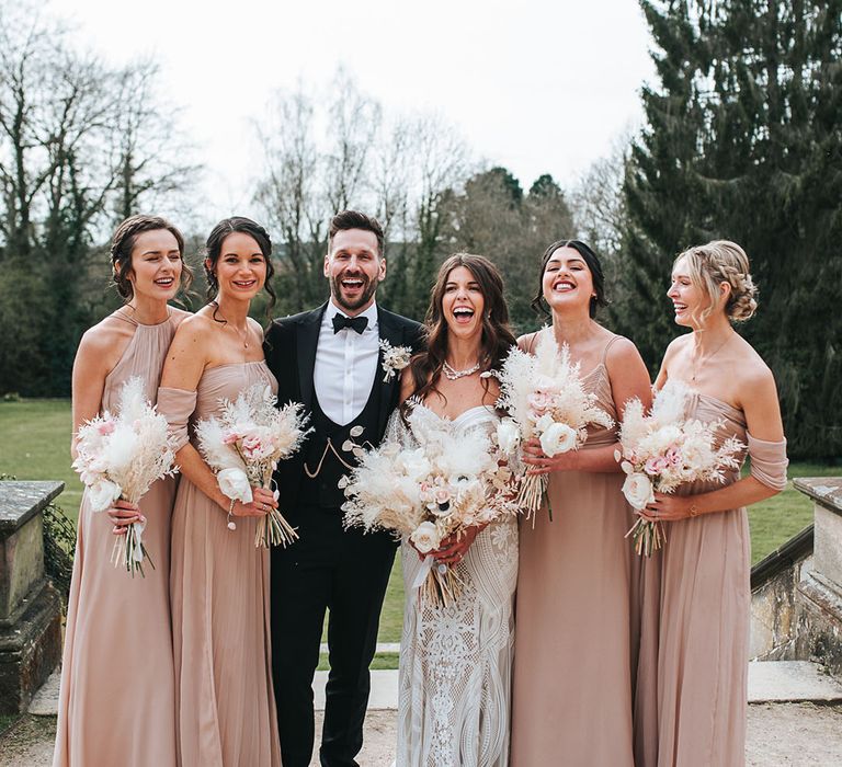 Neutral pink bridesmaid dresses in different styles laughing with the bride and groom for their country wedding at Hampton Manor 