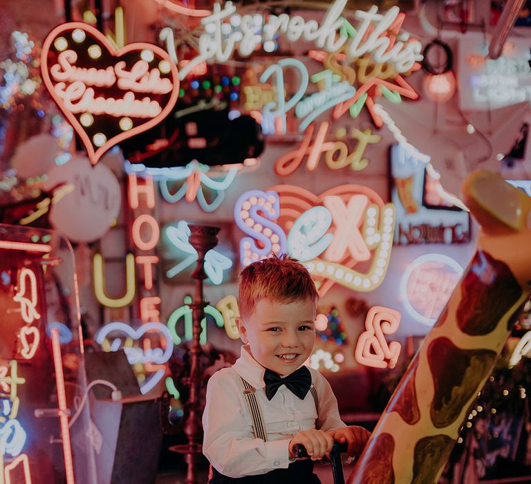 Page boy wearing suspenders and bowtie playing on large wooden giraffe at Gods Own Junkyard 