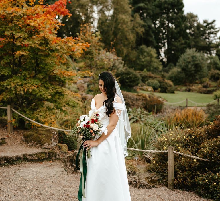 Bride holds white orchid bridal bouquet and wears fingertip length lace edge veil 