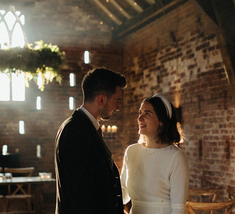 Groom in three piece suit smiles down at the bride in a high neck wedding dress as the sun streams into the Grangefields wedding venue 