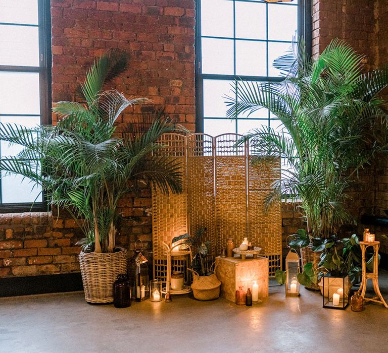 Lush green plants beside wicker partition and pillar candles in lanterns 