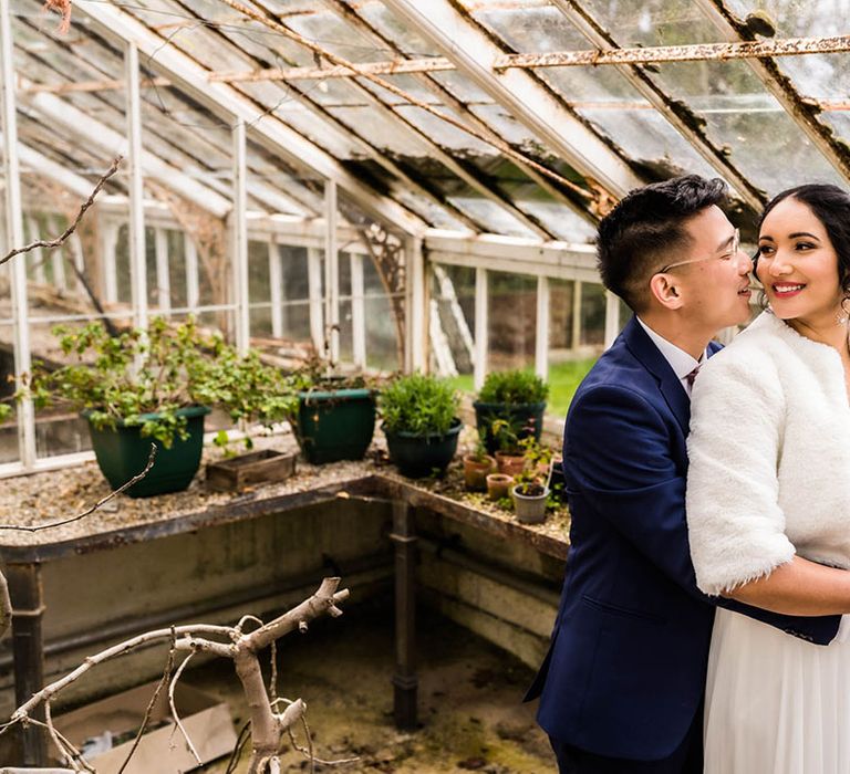 Groom embraces his bride wearing faux fur stole coverup in greenhouse 