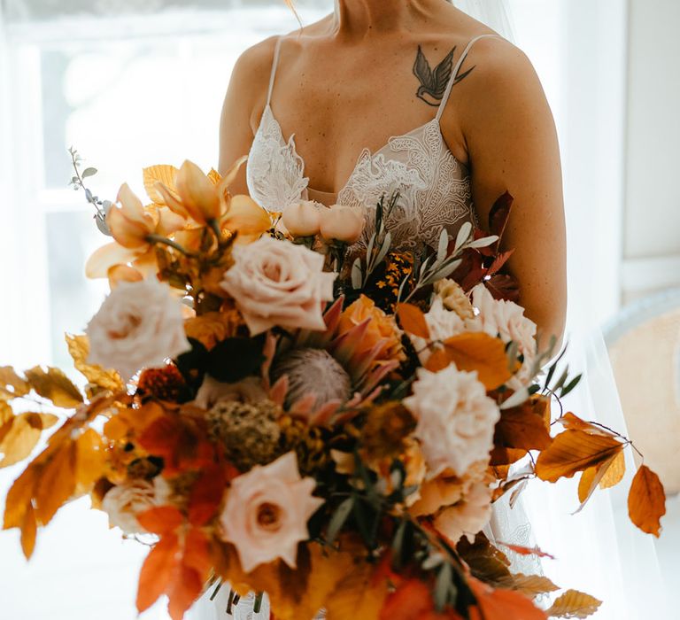 Bride in Madi Lane lace wedding dress holds large burnt orange bridal bouquet complete with pale pink roses and green foliage  