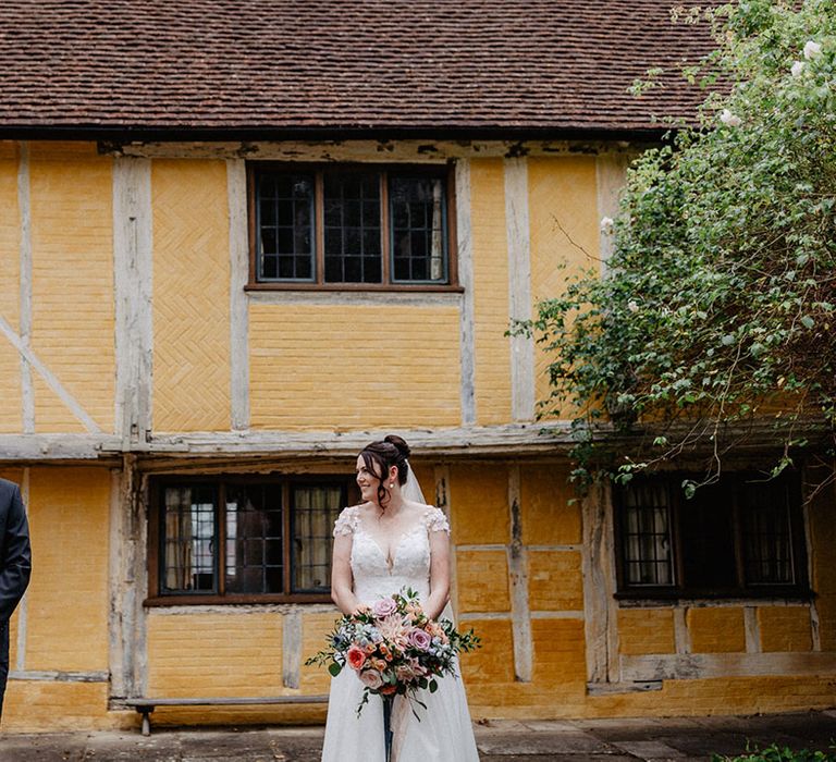 The bride in a flower wedding dress with the groom in front of rustic yellow building for cute couple portraits 