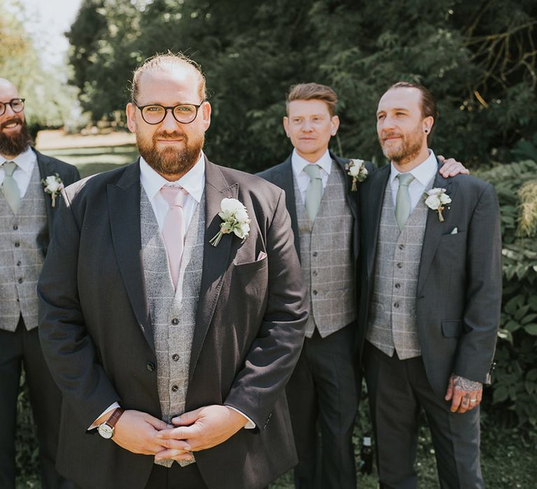 Pastel pink and green wedding theme with the groom wearing a pink tie and grey sit and the groomsmen in matching grey suits with green ties 