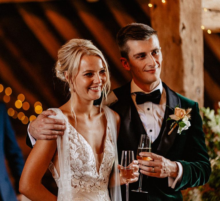 The bride and groom stand drinking champagne together as they listen to the wedding speeches 