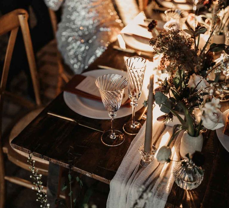 Rustic luxe wedding tablescape with white cloth table runners, foliage, baby's-breath, eucalyptus and dried flower floral arrangements, neutral tapered candles and small ceramic vases 