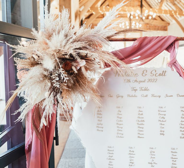 Hexagonal white and rose gold seating plan on copper frame decorated with pampas grass 