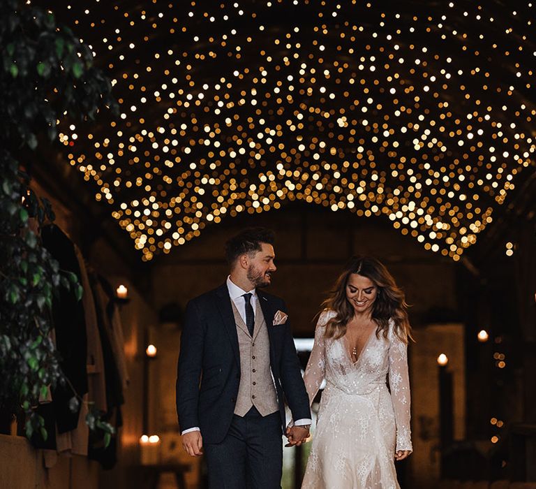 Cosy and rustic lighting at the barn wedding venue with the bride in a sparkly winter wedding dress and groom in three piece suit