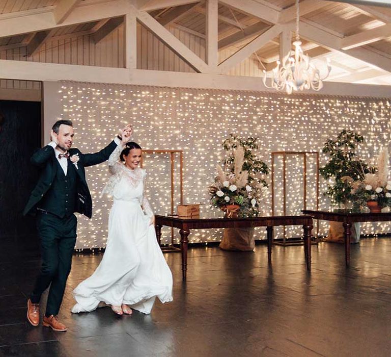 bride and groom entering the wedding reception with a fairy light curtain wedding backdrop 