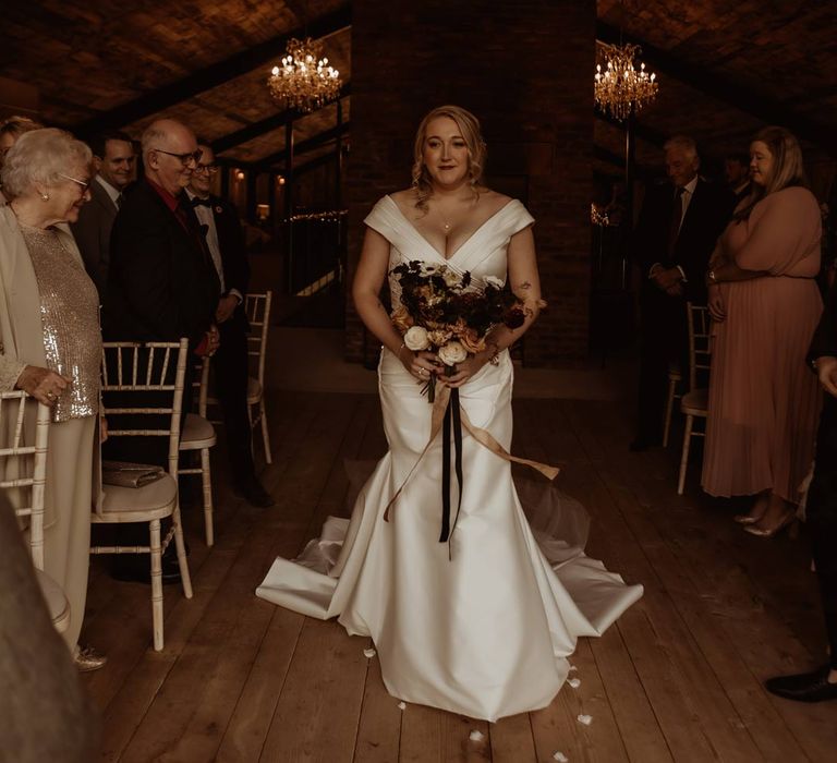 Bride in satin short sleeve deep v wedding dress and church length veil walking down the aisle holding white, dusky pink and burnt red dried flower, rose and peony bridal bouquet 