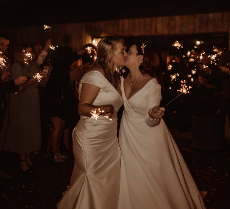 Bride in long sleeve deep v wedding dress and church length veil and bride in satin short sleeve deep v wedding dress and church length veil doing wedding sparkler send off at Hidden River Cabins 