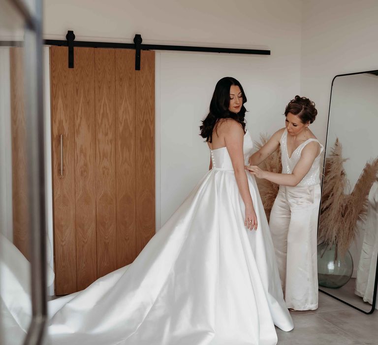 Maid of honour helping the bride in a Suzanne Neville wedding dress get ready 