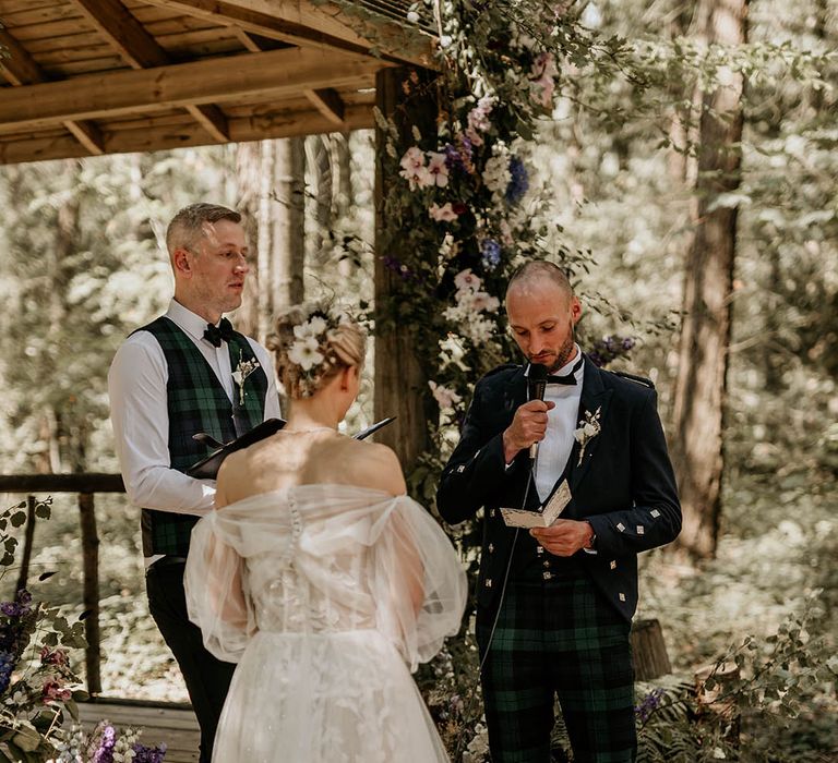 Bride in a Milla Nova wedding dress with detachable sleeves with groom wearing green checkered trousers reading out his wedding vows 