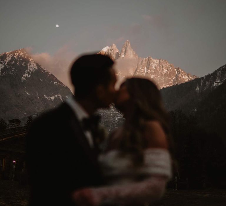 Bride and groom kissing in front of the French Alps at destination ski wedding