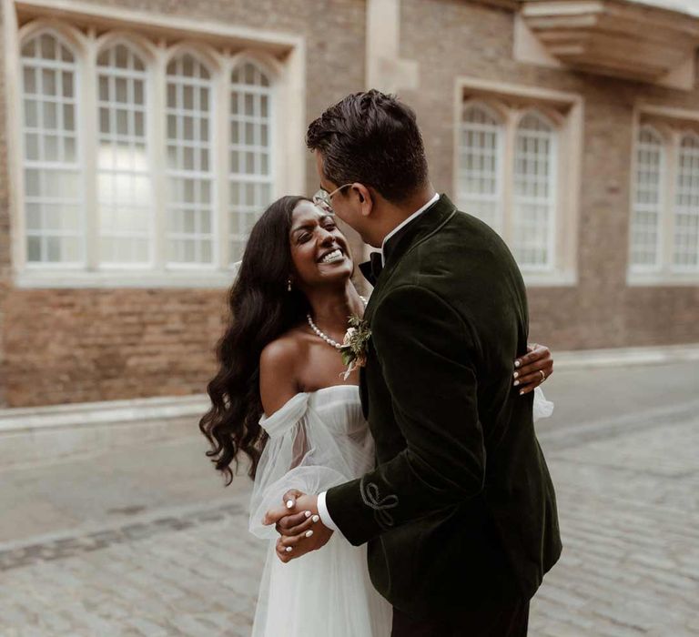 Groom in bottle green velvet grooms suit dancing with bride in off the shoulder layered tulle wedding dress in the streets of London