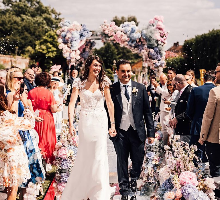 The bride and groom walk back down the mirrored wedding aisle as a married couple to confetti 