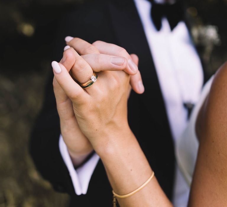 Bride wearing oval diamond engagement ring and gold wedding band in black tuxedo 