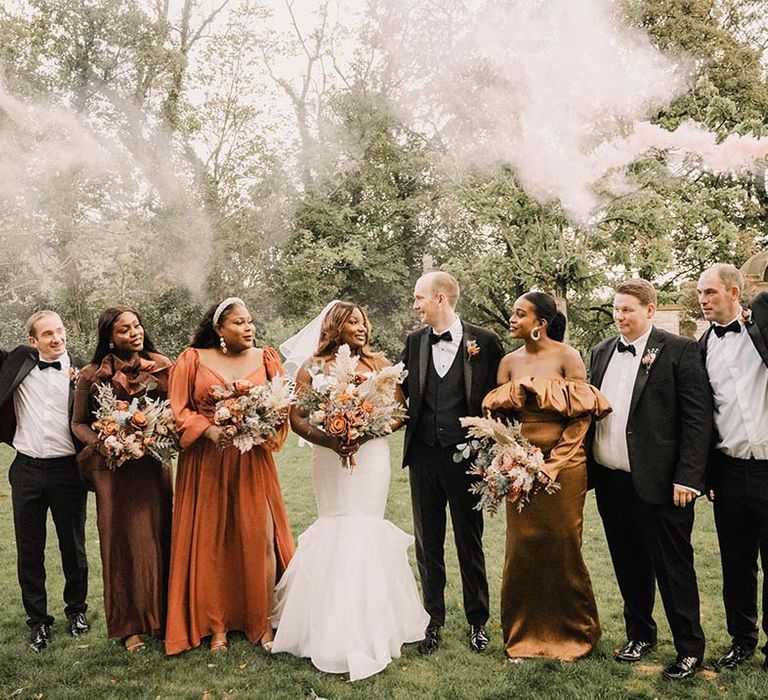 Smoke flare epic wedding party photo with bridesmaids wearing brown and metallic autumn bridesmaid dresses and groomsmen in black tuxedos 