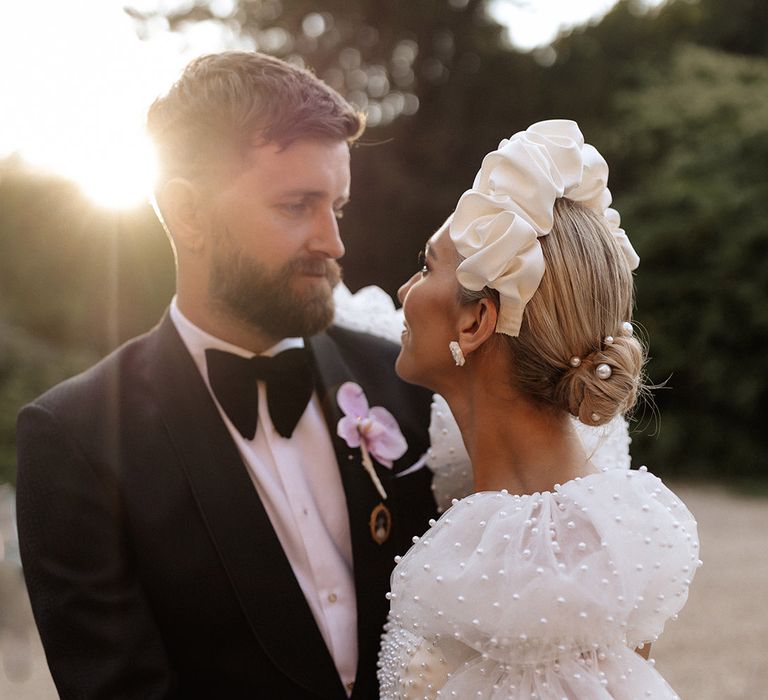 Golden hour couple portrait with groom in black tuxedo and bride in pearl puff sleeve reception dress 