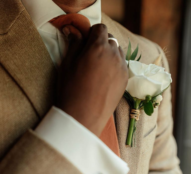 Groom in beige neutral suit with white flower buttonhole and colourful orange tie 