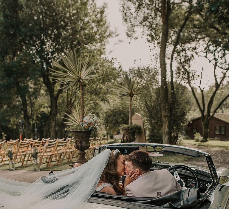 The bride and groom share a kiss as they ride in their vintage wedding car at rustic luxe wedding 