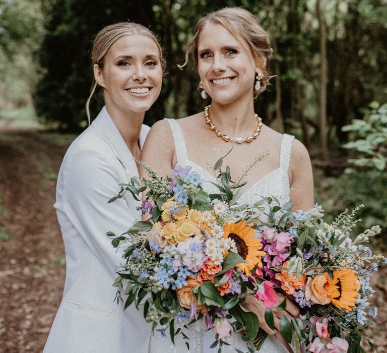 Brides smile together as they pose for couple portraits at their woodland wedding in Norfolk 