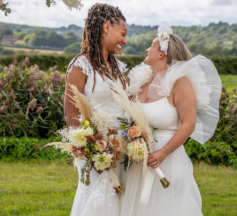 Two brides smile at each other at their festival tipi wedding 