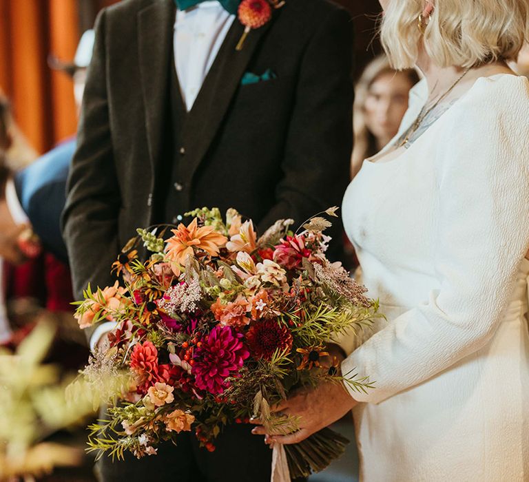 Bride holding natural autumnal wedding bouquet at registry office wedding in short wedding dress 