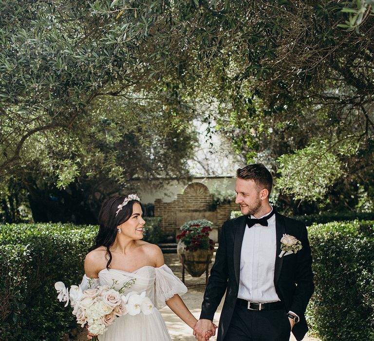 Bride and groom walk hand in hand at their outdoor destination wedding in Southern Spain 