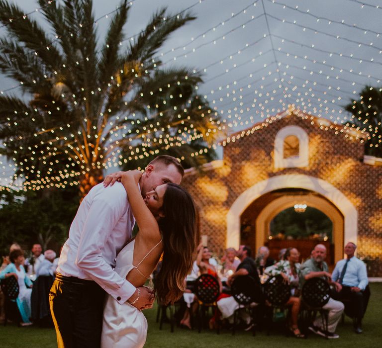 The bride and groom dance on a lit up outdoor dance floor at dusk