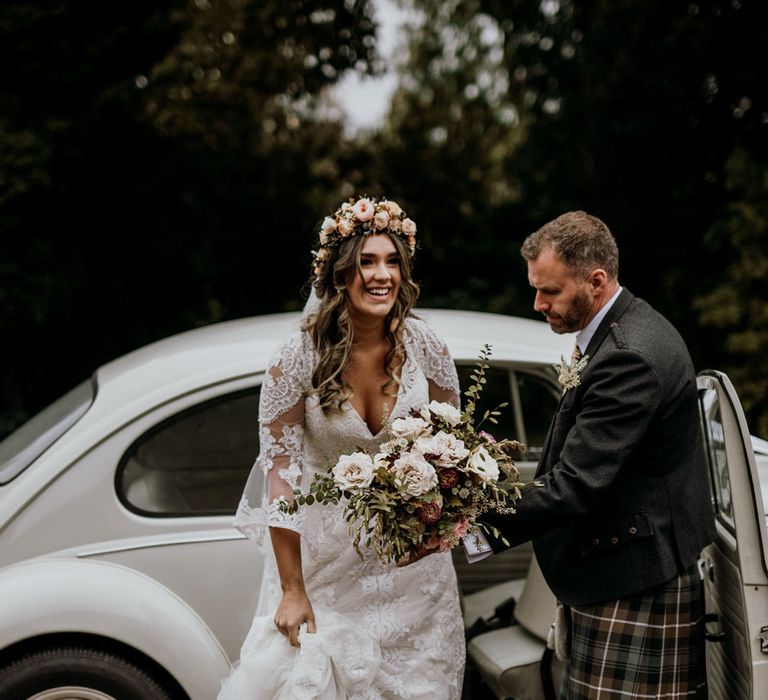 Boho bride with white rose bouquet and pink rose flower crown gets out of white vintage wedding car