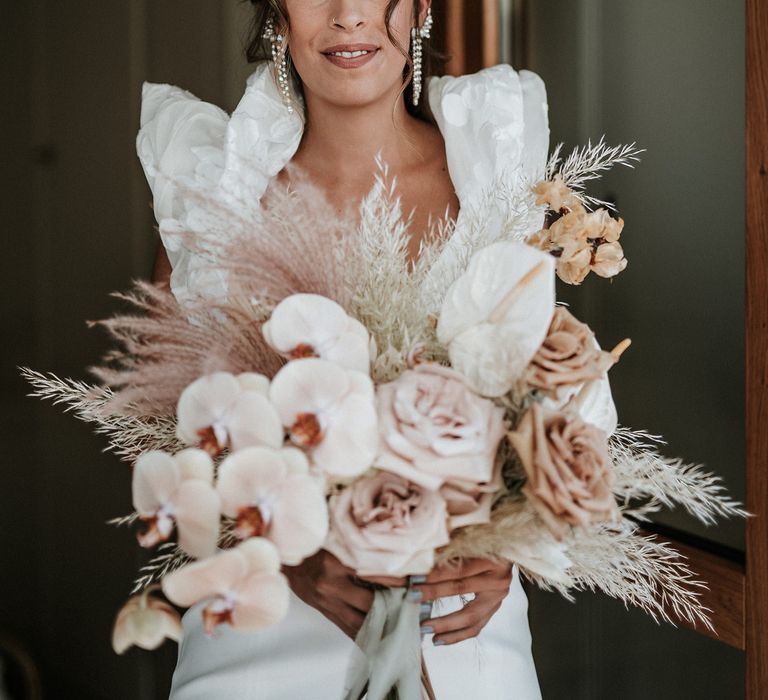 Destination bride holding a dusky pink and peach wedding bouquet with orchids, roses, anthuriums, and pampas grass. 