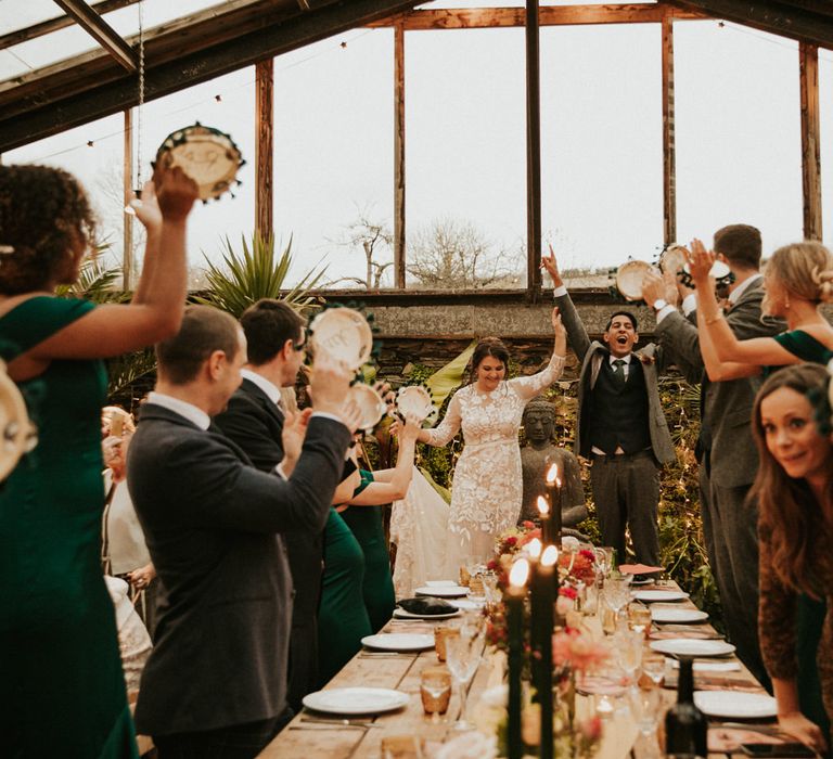 Bride and groom entering their glasshouse wedding reception with guests banging their tambourine wedding favours 