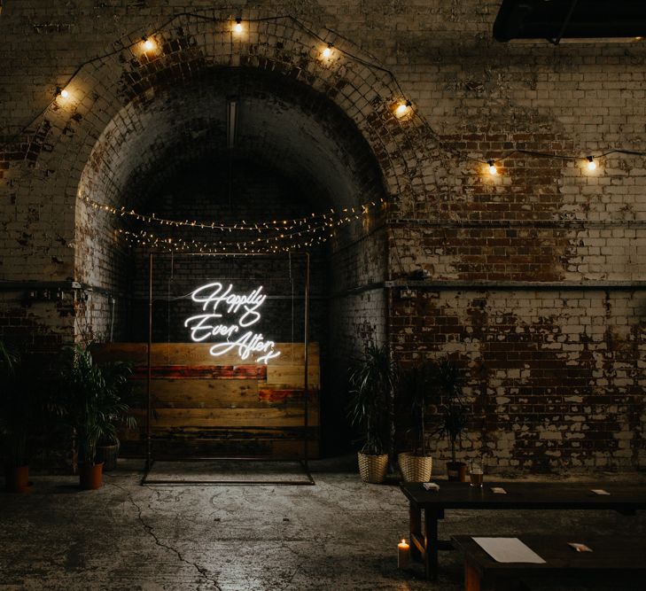 Industrial venue shot with 'happily ever after' neon sign and hanging lights against exposed brick walls.