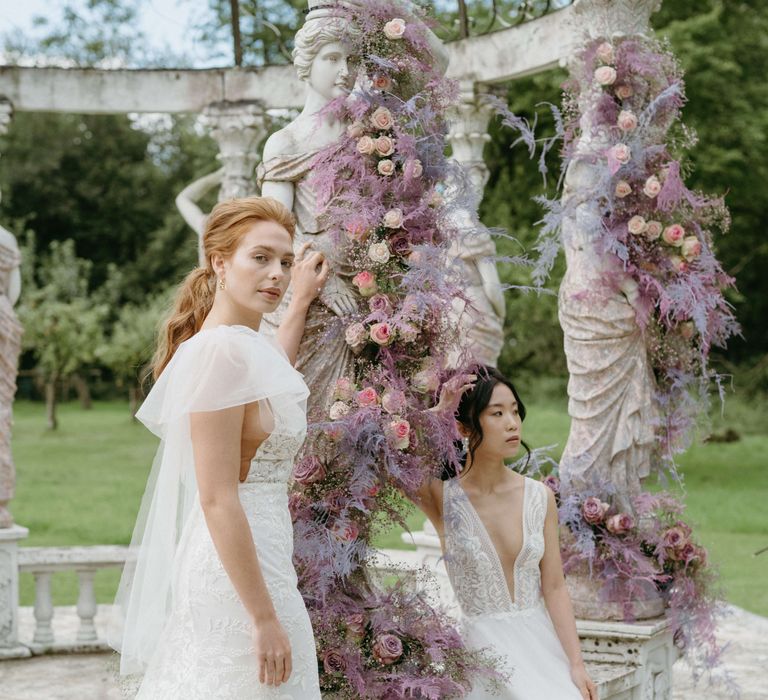 Brides pose together in front of bandstand surrounded by lilac florals