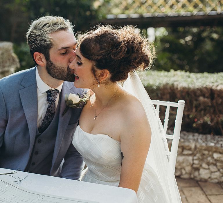 Groom in a light blue suit kissing his bride in a strapless wedding dress at their intimate Gibraltar Botanic Gardens elopement