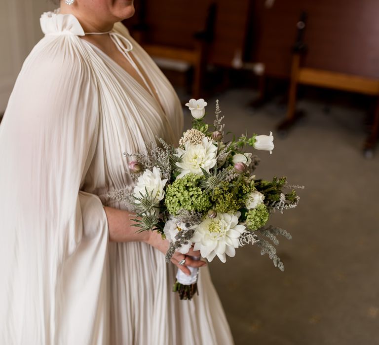 Bride in a long sleeve wedding dress with ruffles holding a white and green wedding bouquet 