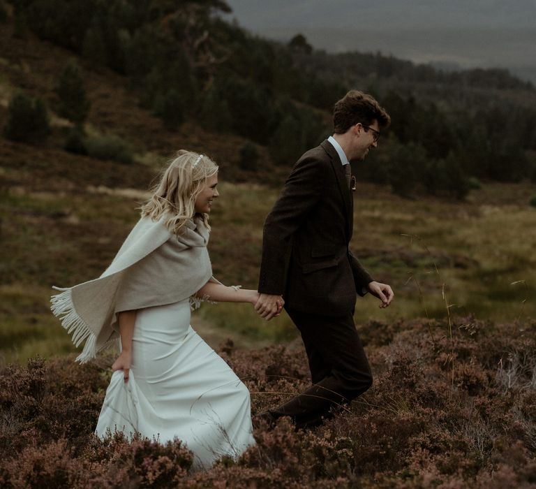 Bride & groom walk through the hills whilst holding hands