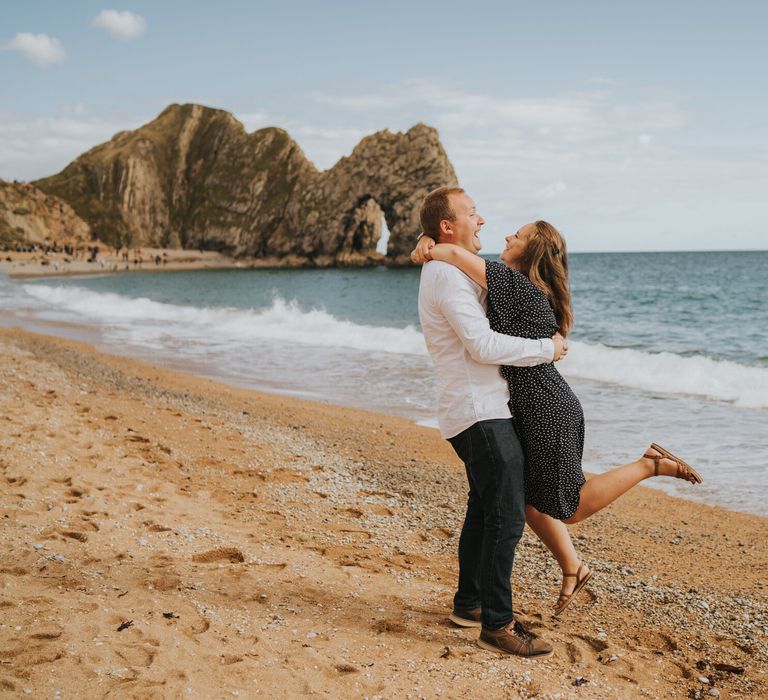 Groom to be holding his bride to be at durdle door bay beach