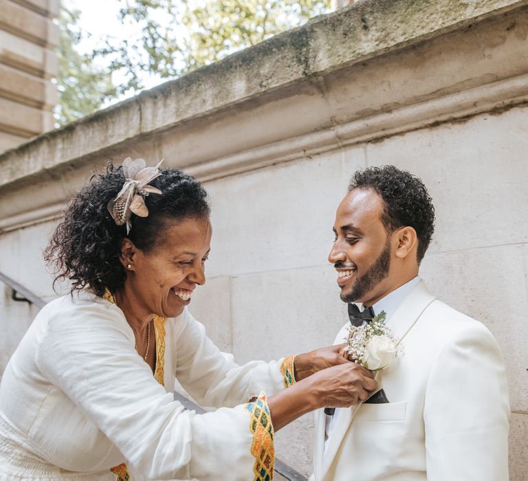 Mother of the groom putting on the grooms white rose and gypsophila buttonhole 