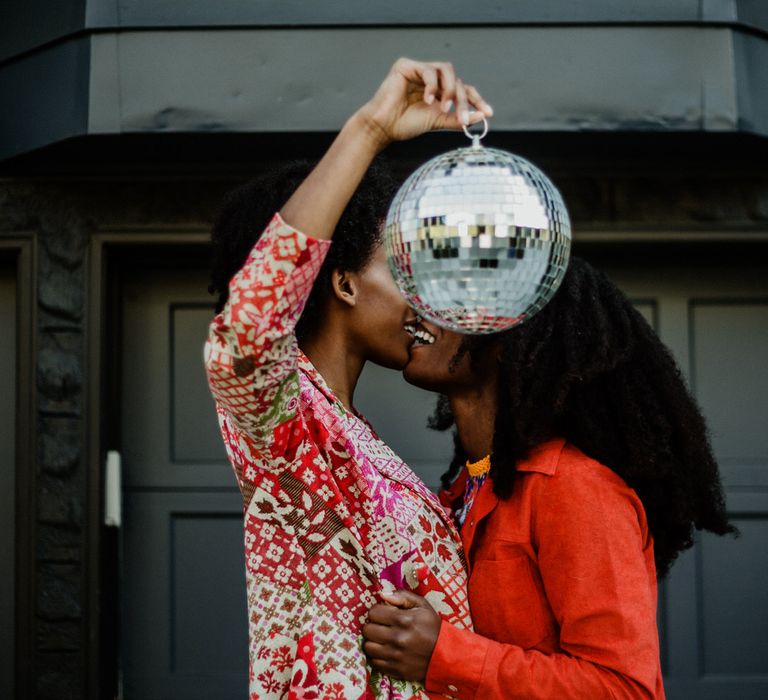 Black LGBTQ+ couple kissing behind a glitter ball at their engagement session 