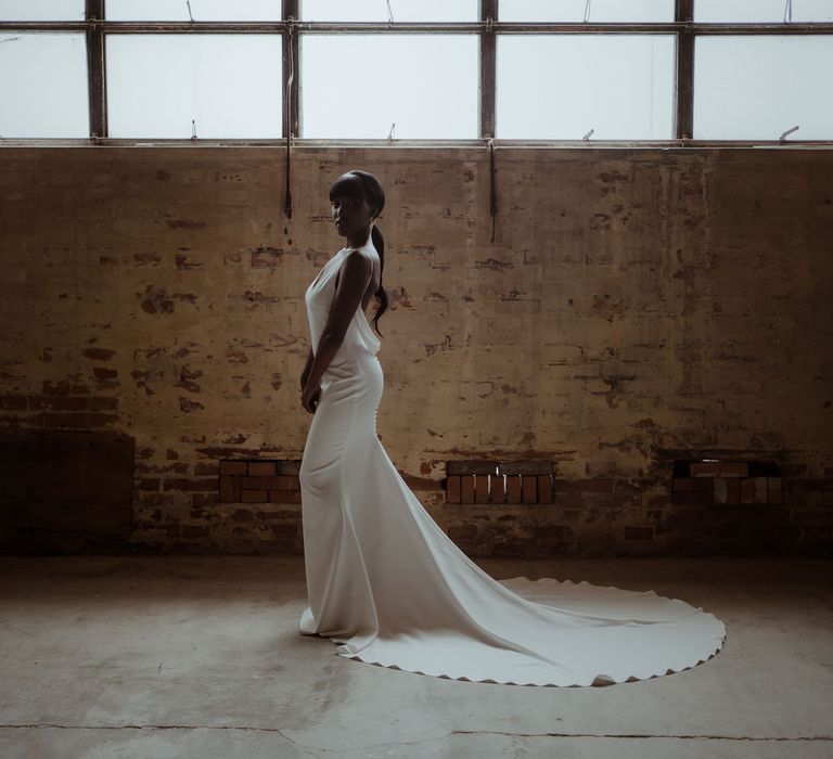 A bride stands to the side showing off the train on her simple white wedding dress for a simple elegant wedding.