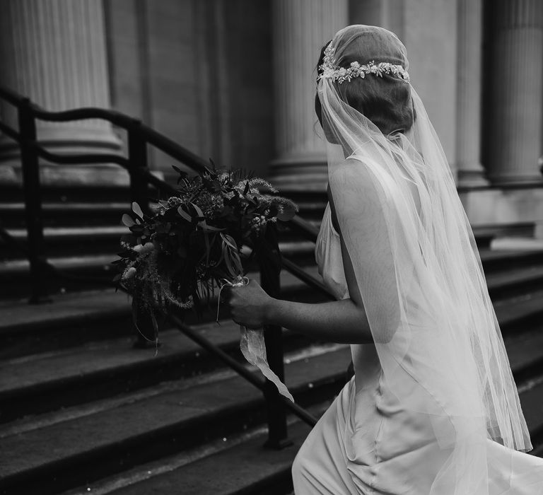 Black and white portrait of a bride in a ghost wedding dress walking up the steps of Old Marylebone town hall wearing a Juliet cap wedding veil 